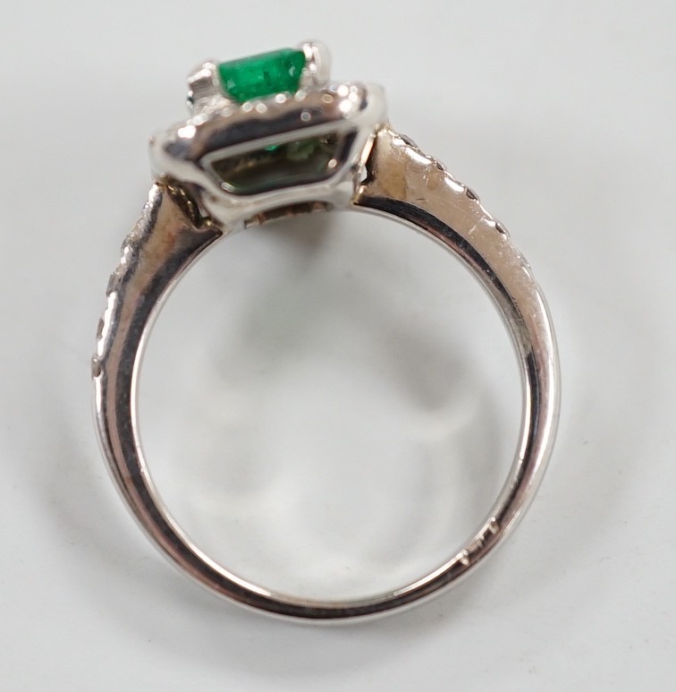 A modern 750 white metal, emerald and diamond set octagonal cluster ring, with diamond set shoulders, size J, gross weight 4.9 grams.